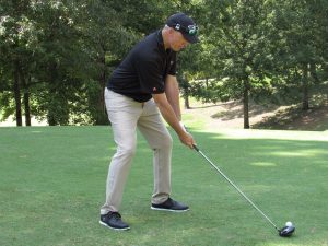 A golfer in black shirt and tan pants starts a swing