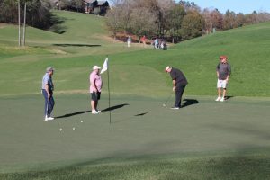 Four golfers gathered around a hole with flag still in it