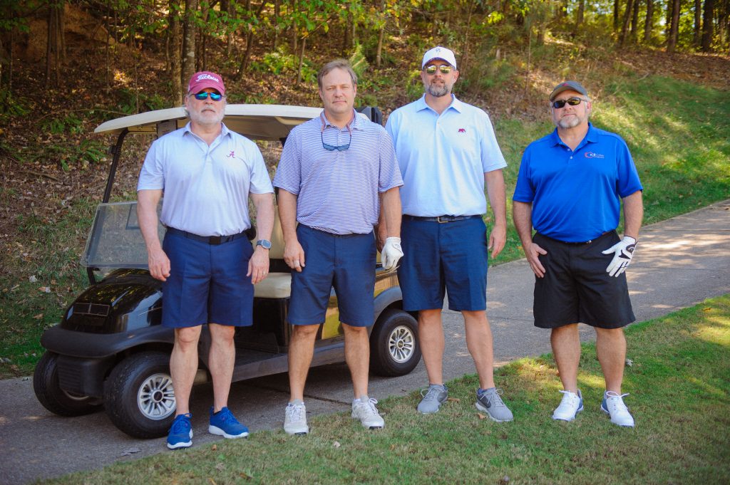 4 guys stand beside a golf cart