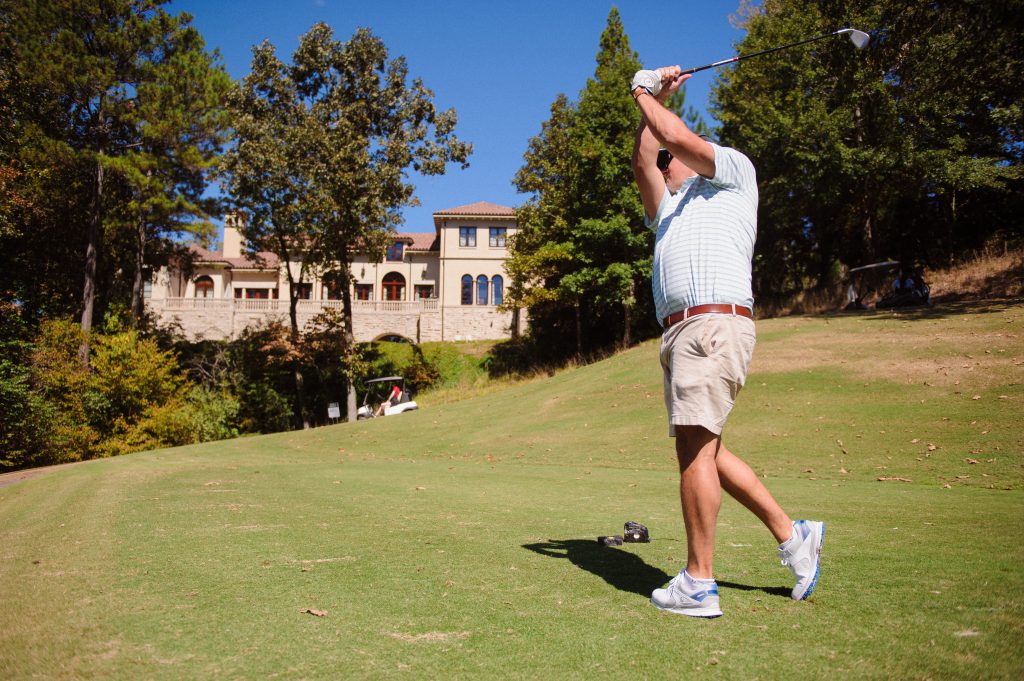 a golfer swinging with a building in the background