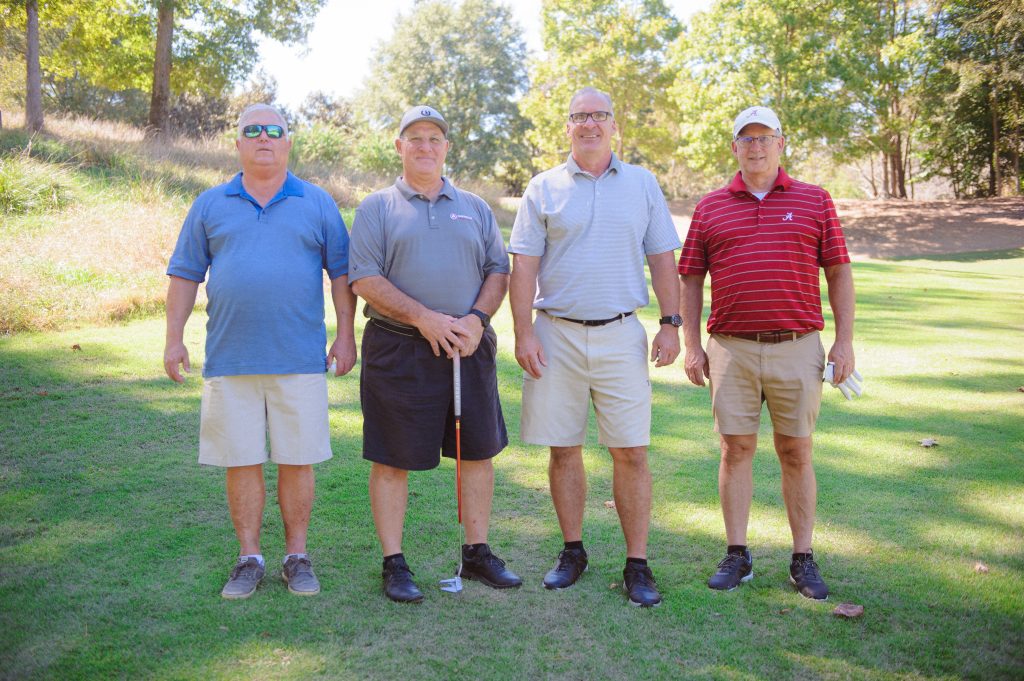 4 guys, 1 in blue shirt, 1 in red shirt, standing on a golf course