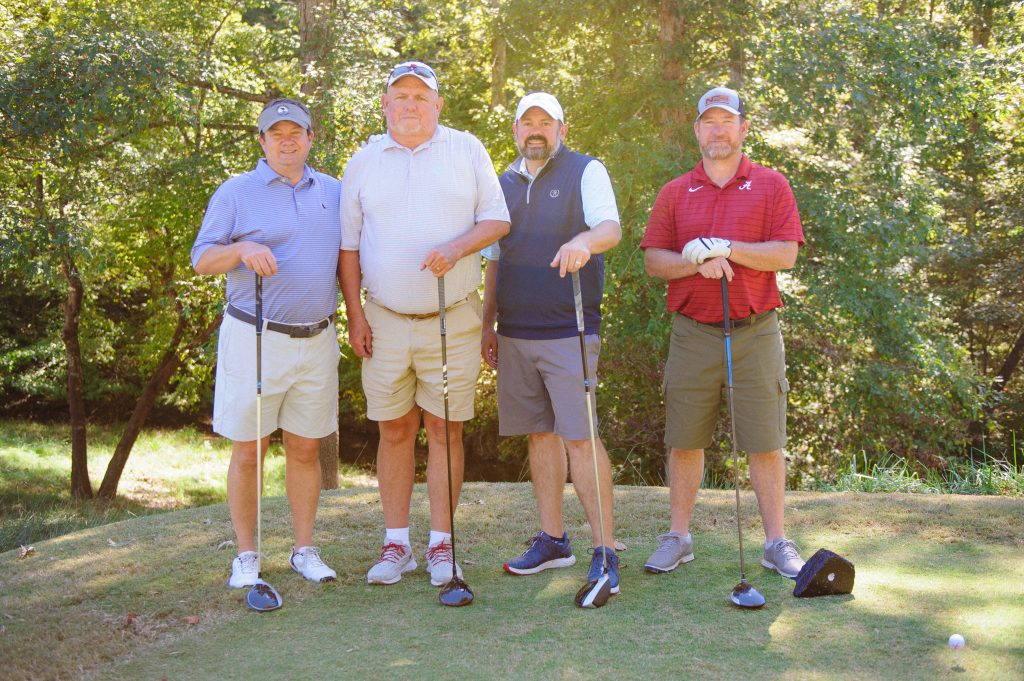 4 guys with golf clubs, 1 in a red shirt and another in a blue shirt with white sleeves