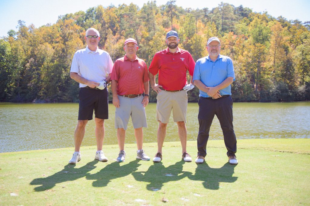 4 guys in front of a water area on the golf course